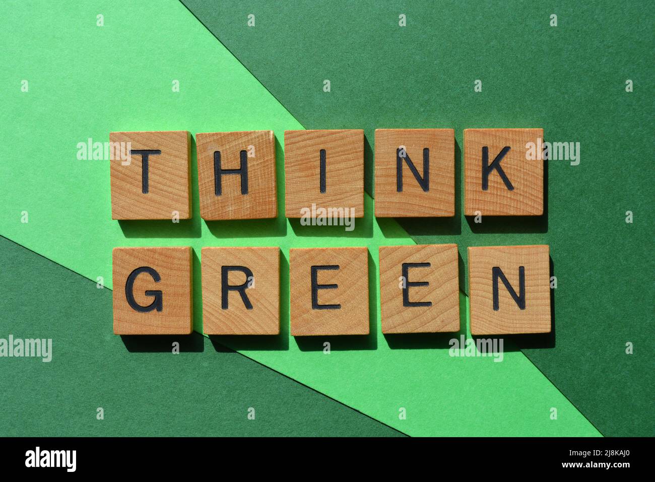Think Green, Wörter in Holzbuchstaben isoliert auf grünem Hintergrund Stockfoto
