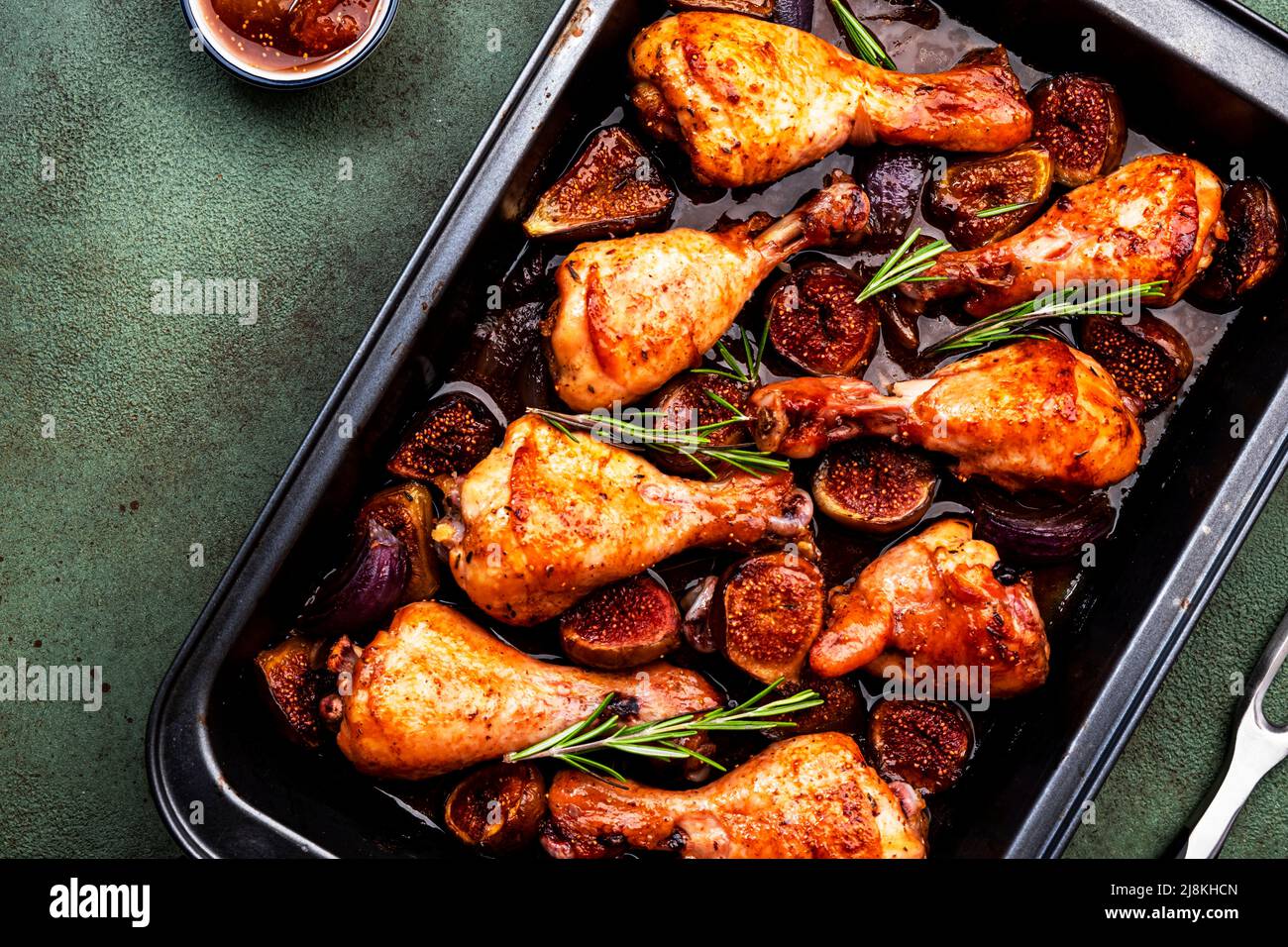 Gebackene Hähnchenbeine, Drumsticks mit süßen Feigen und Zwiebeln in balsamischer Marinade auf schwarzem Backblech, rostiger grüner Tischhintergrund, Draufsicht Stockfoto