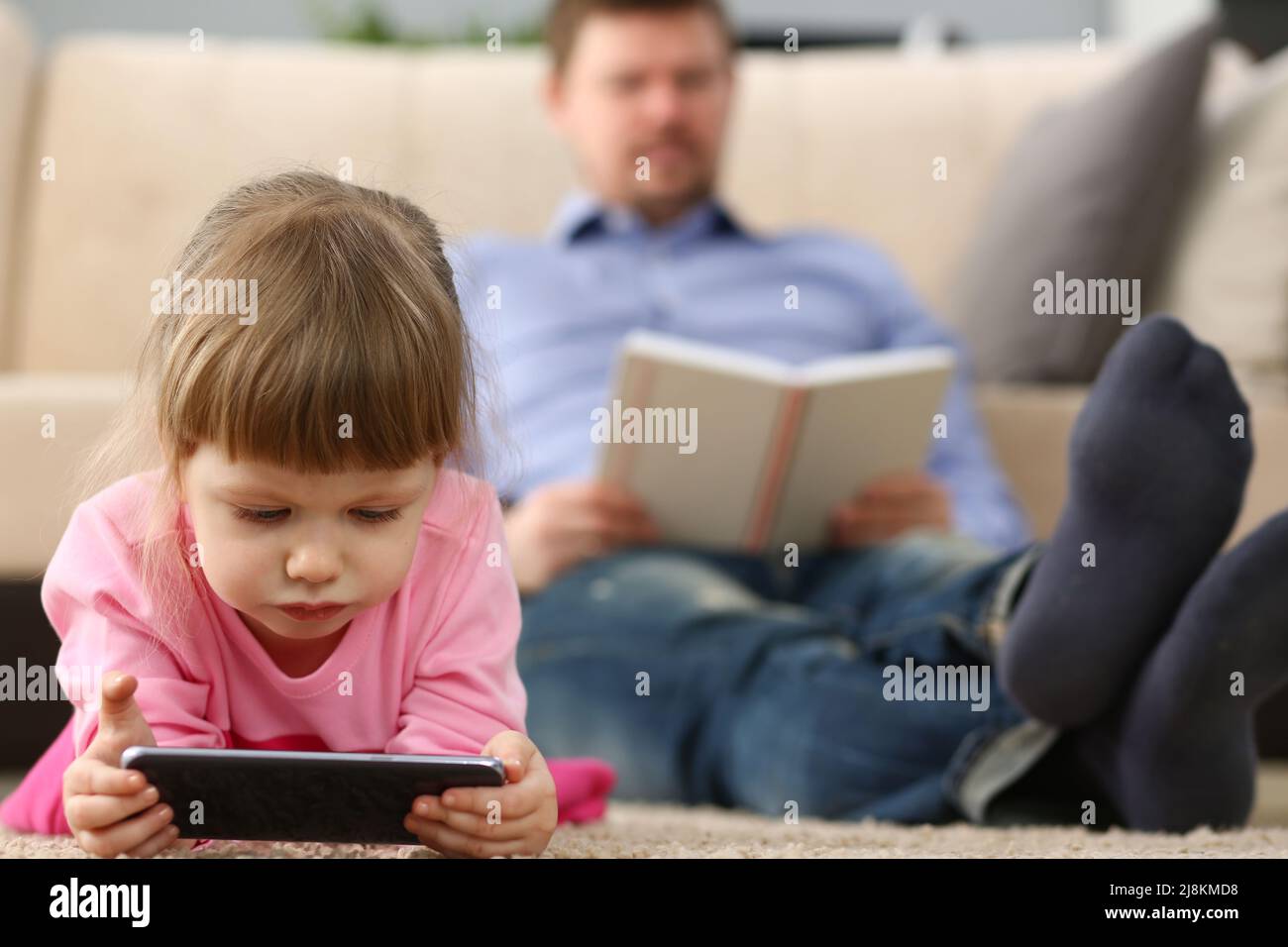 Kleine Mädchen spielen mit Smartphone-Gerät, digitale Unterhaltung für Kinder, Vater Buch zu lesen Stockfoto