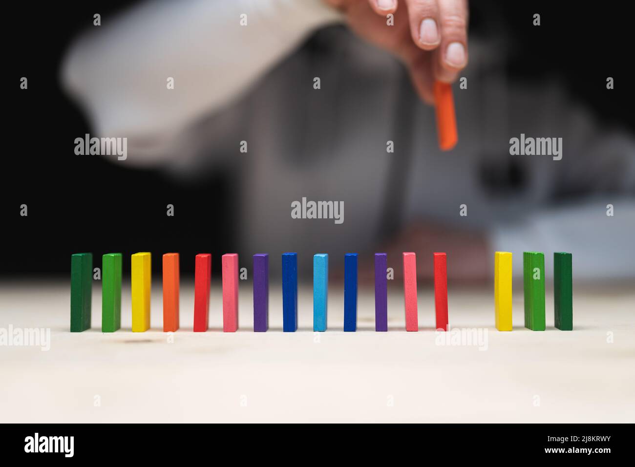 Konzeptionelles Foto einer Hand, die einen Stein auf eine Reihe von Domino-Steinen legt. Domino-Effekt mit farbigen Steinen und Copyspace Stockfoto