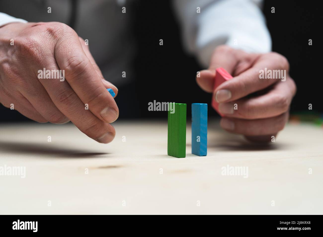 Konzeptionelles Foto von Händen, die eine Reihe von Domino-Steinen vorbereiten. Domino-Effekt mit farbigen Steinen und Copyspace Stockfoto