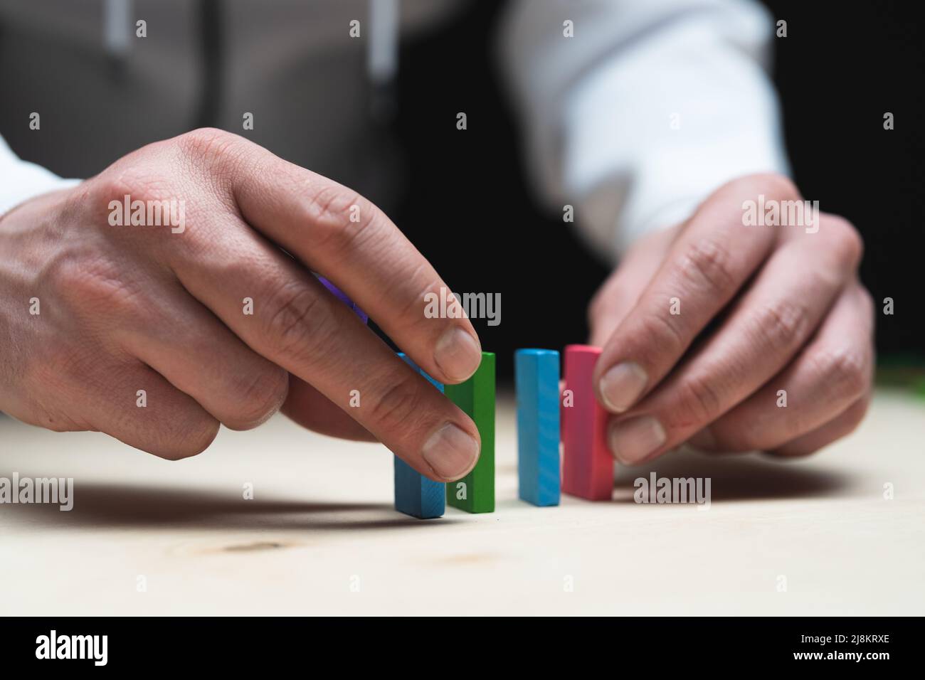 Konzeptionelles Foto von Händen, die eine Reihe von Domino-Steinen vorbereiten. Domino-Effekt mit farbigen Steinen und Copyspace Stockfoto