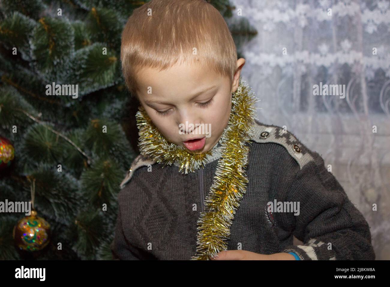 Junge mit weihnachtlicher Lametta am Hals in den Häusern in der Nähe der Tanne Stockfoto