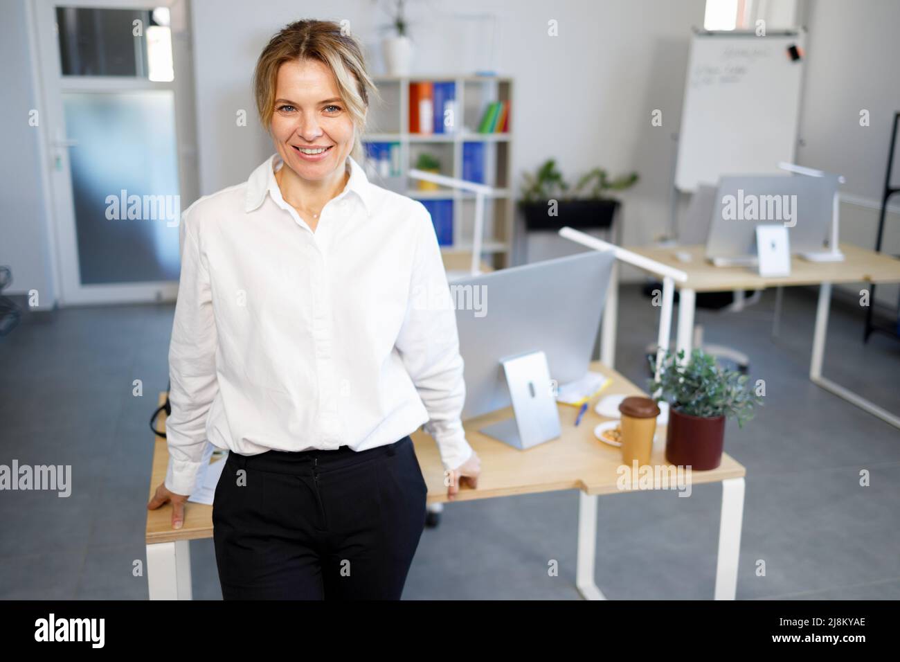 Porträt einer attraktiven erwachsenen Bürofrau, die sich an ihren Schreibtisch lehnt Stockfoto