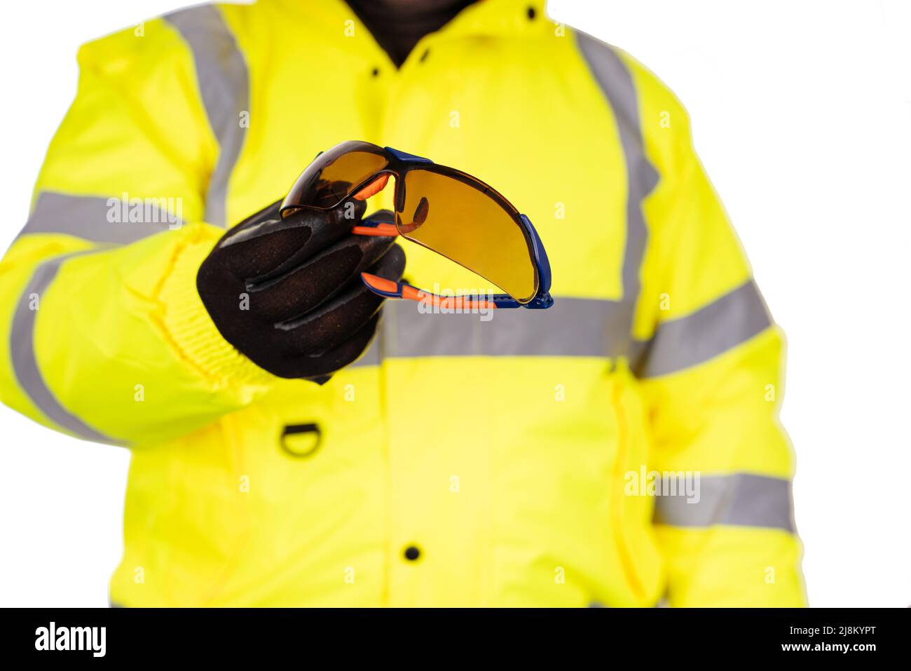 Ein Bauarbeiter in einem gelben Hi-viz-Mantel auf weißem Hintergrund gibt dem Betrachter eine dunkel getönte Schutzbrille. Tragen Sie zum Schutz eine Schutzbrille Stockfoto