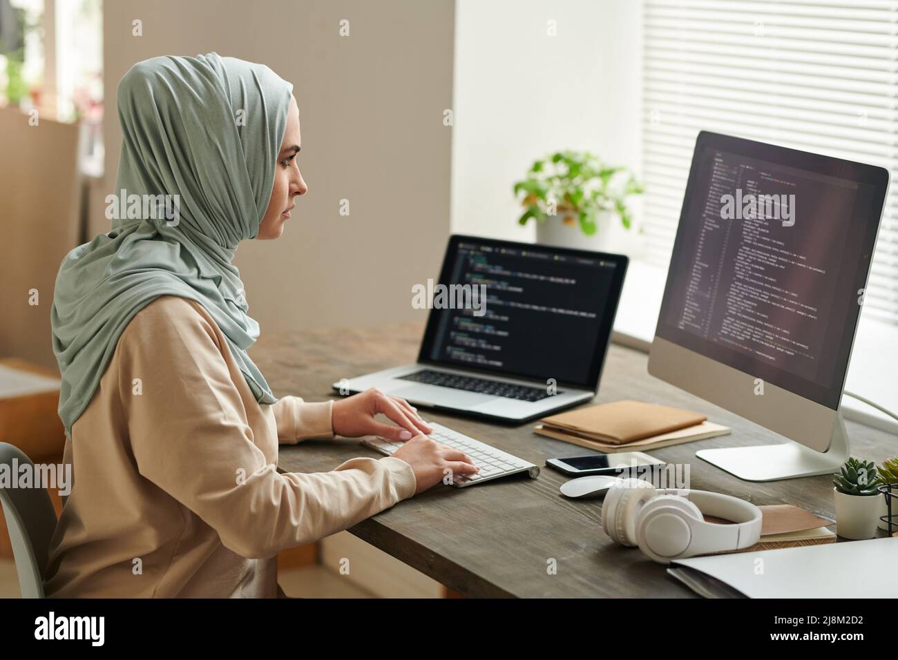 Erfolgreiche Frau aus dem Nahen Osten trägt einen hellblauen Hijab und sitzt am Schreibtisch, um an Computercode und Kopierraum zu arbeiten Stockfoto