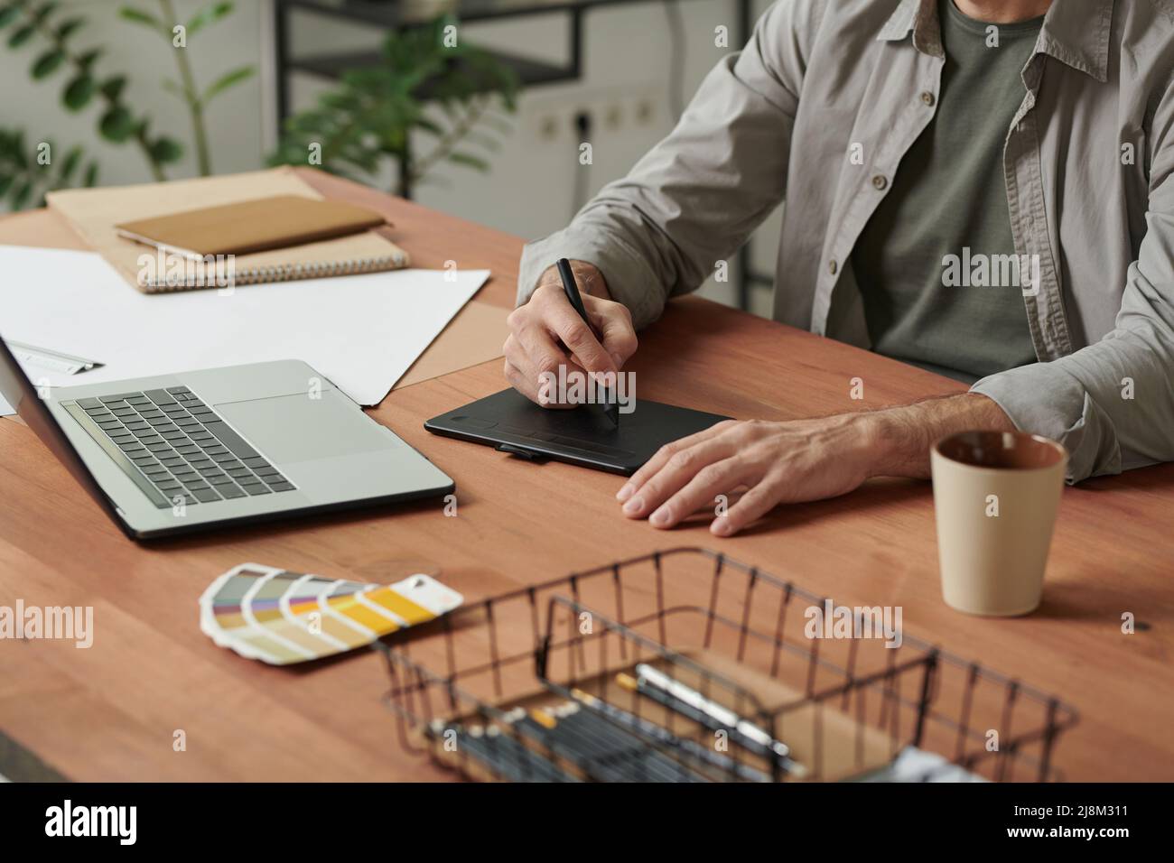 Nahaufnahme eines nicht erkennbaren Grafikers, der mit einem Laptop und Skizzen am Schreibtisch sitzt und im Büro einen Digitalisierer zeichnet Stockfoto