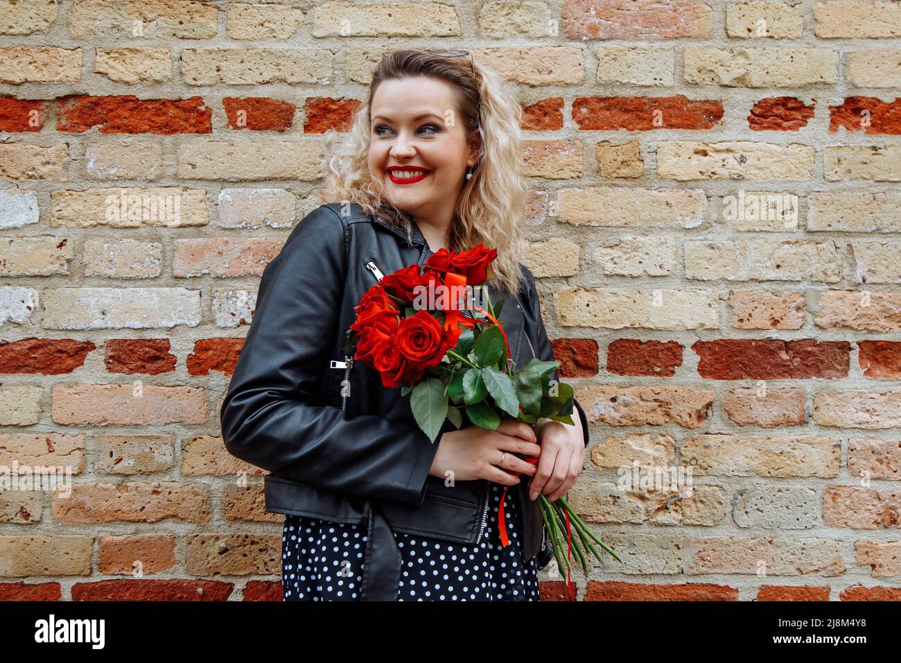 Froh und glücklich blonde Frau auf Datum mit eleganten Rosenblütenstrauß als Geschenk. Glückwunschveranstaltung, Feiertagsjubel Stockfoto