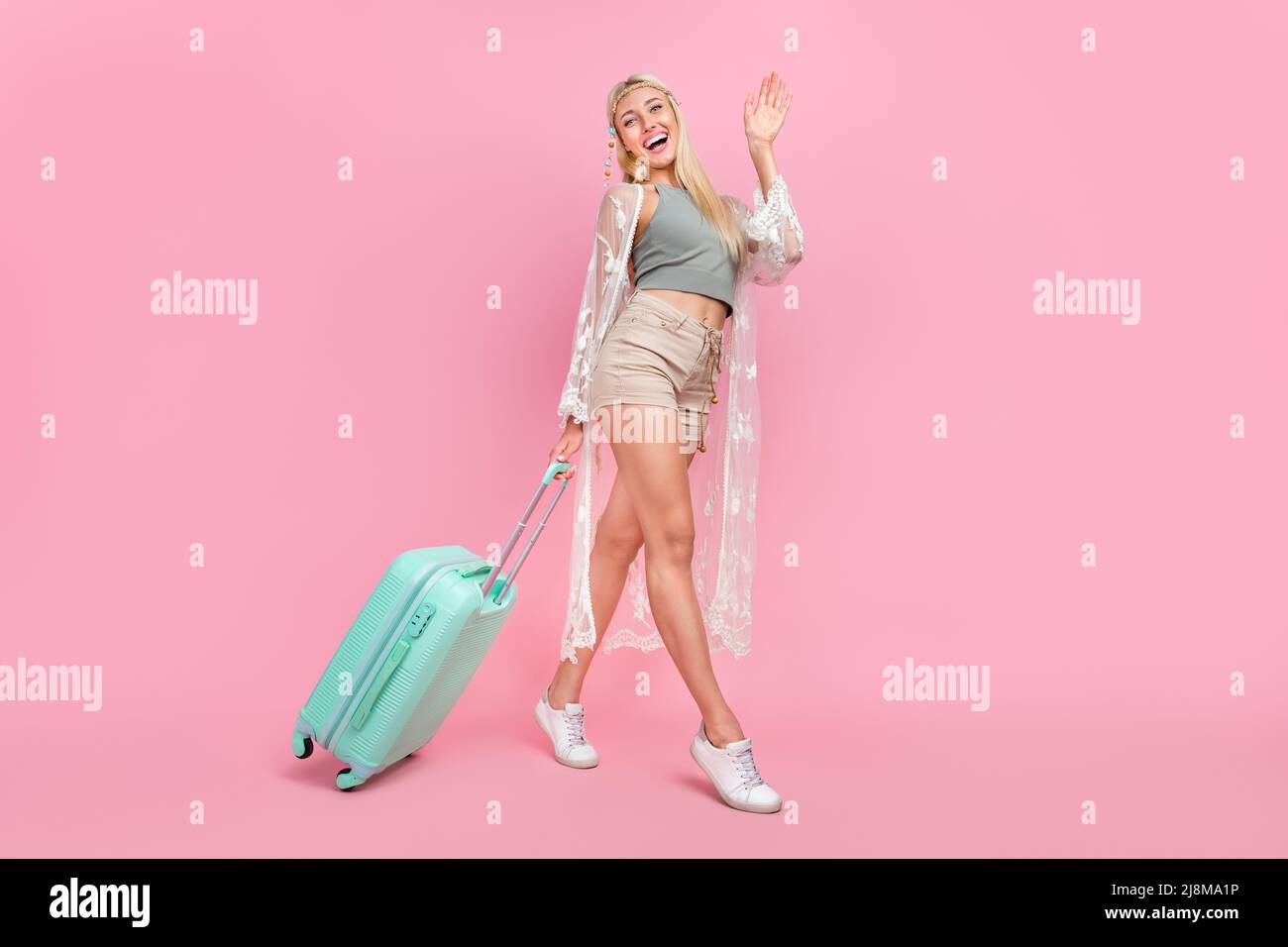 In voller Länge Foto von jungen blonden Dame gehen mit Tasche Welle tragen oben Umhang Shorts Schuhe isoliert auf rosa Hintergrund Stockfoto