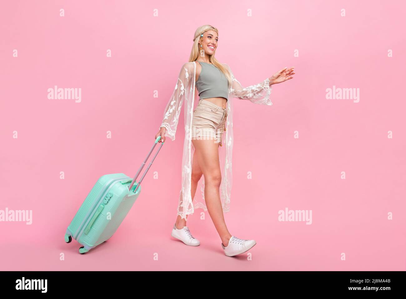 Ganzkörper-Foto von Millennial blonde Dame gehen mit Tasche tragen oben Umhang Shorts Sneakers isoliert auf rosa Hintergrund Stockfoto