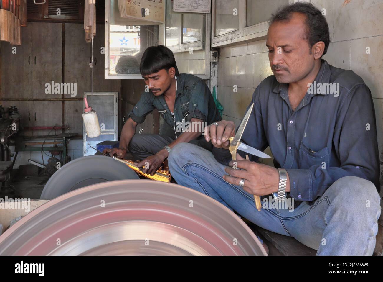 Funken fliegen, als zwei Handwerker in einer Werkstatt in Mumbai, Indien, mechanisch betätigte Radlappräder zum Schärfen von Scheren und Messern einsetzen Stockfoto