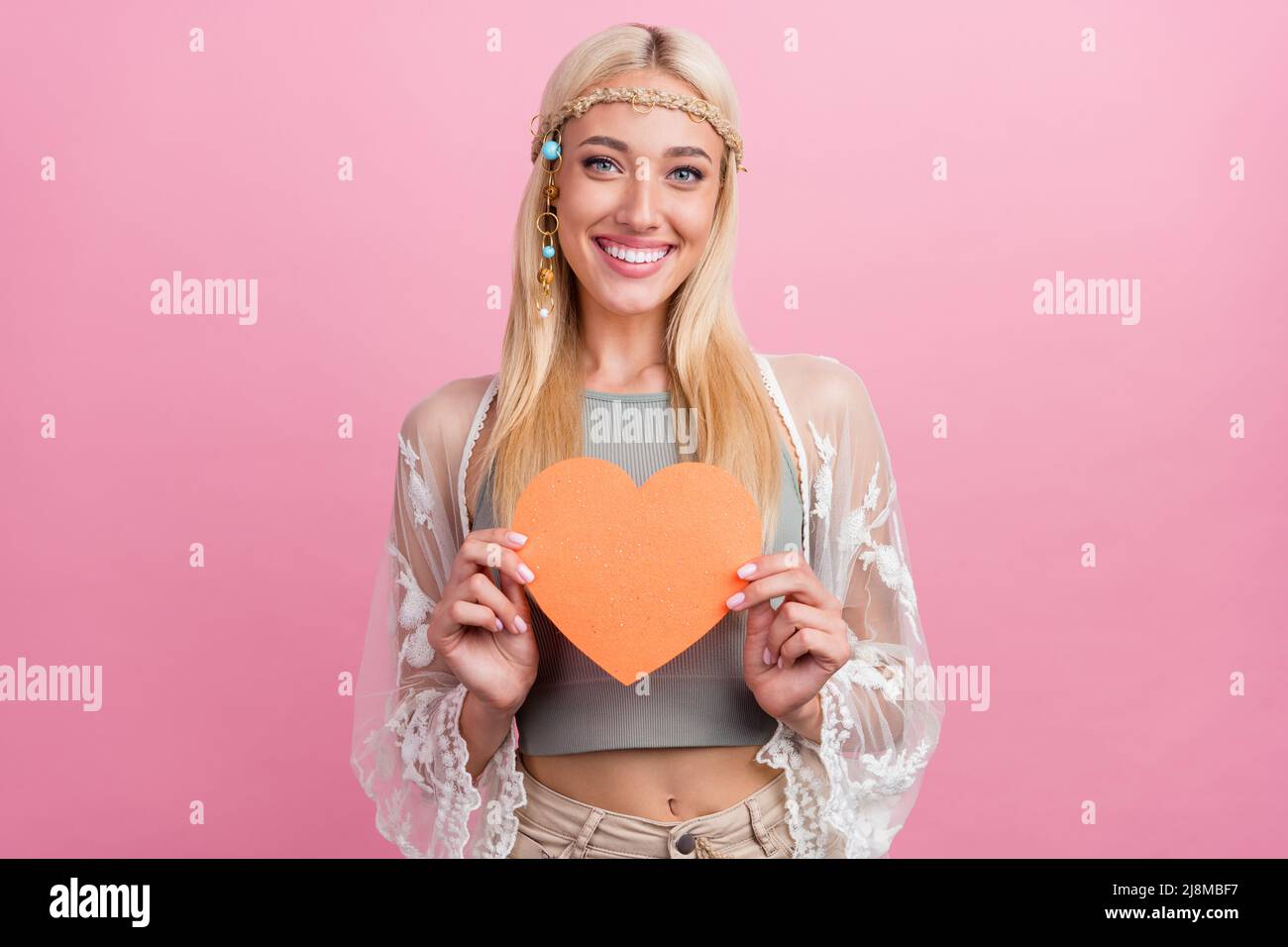 Foto von cool Millennial blonde Dame halten Herz tragen Accessoires oben Umhang isoliert auf rosa Hintergrund Stockfoto