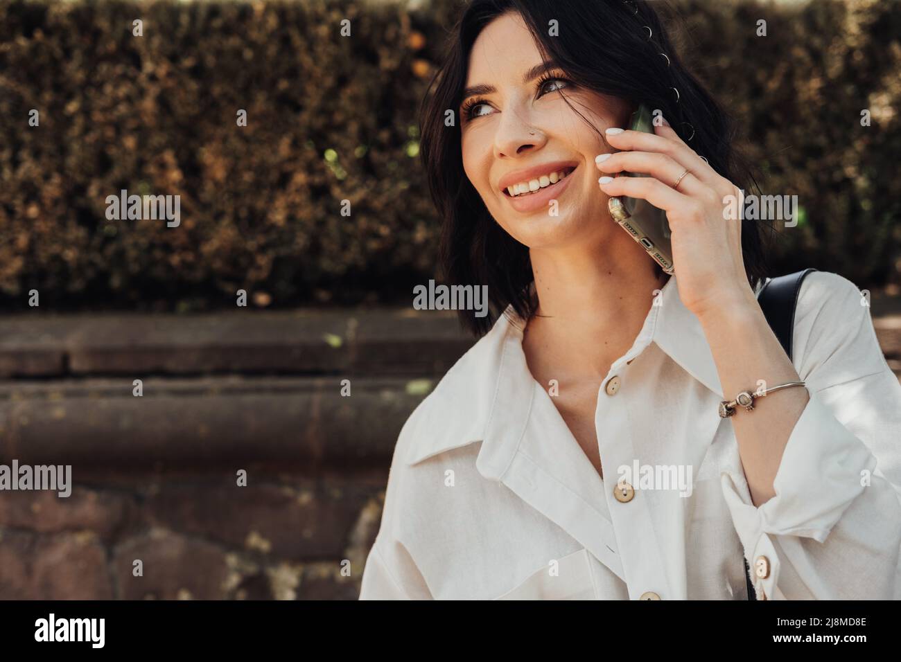 Fröhliche junge Brünette Frau, die im Freien einen Telefonanruf auf dem Smartphone macht, Raum kopieren Stockfoto