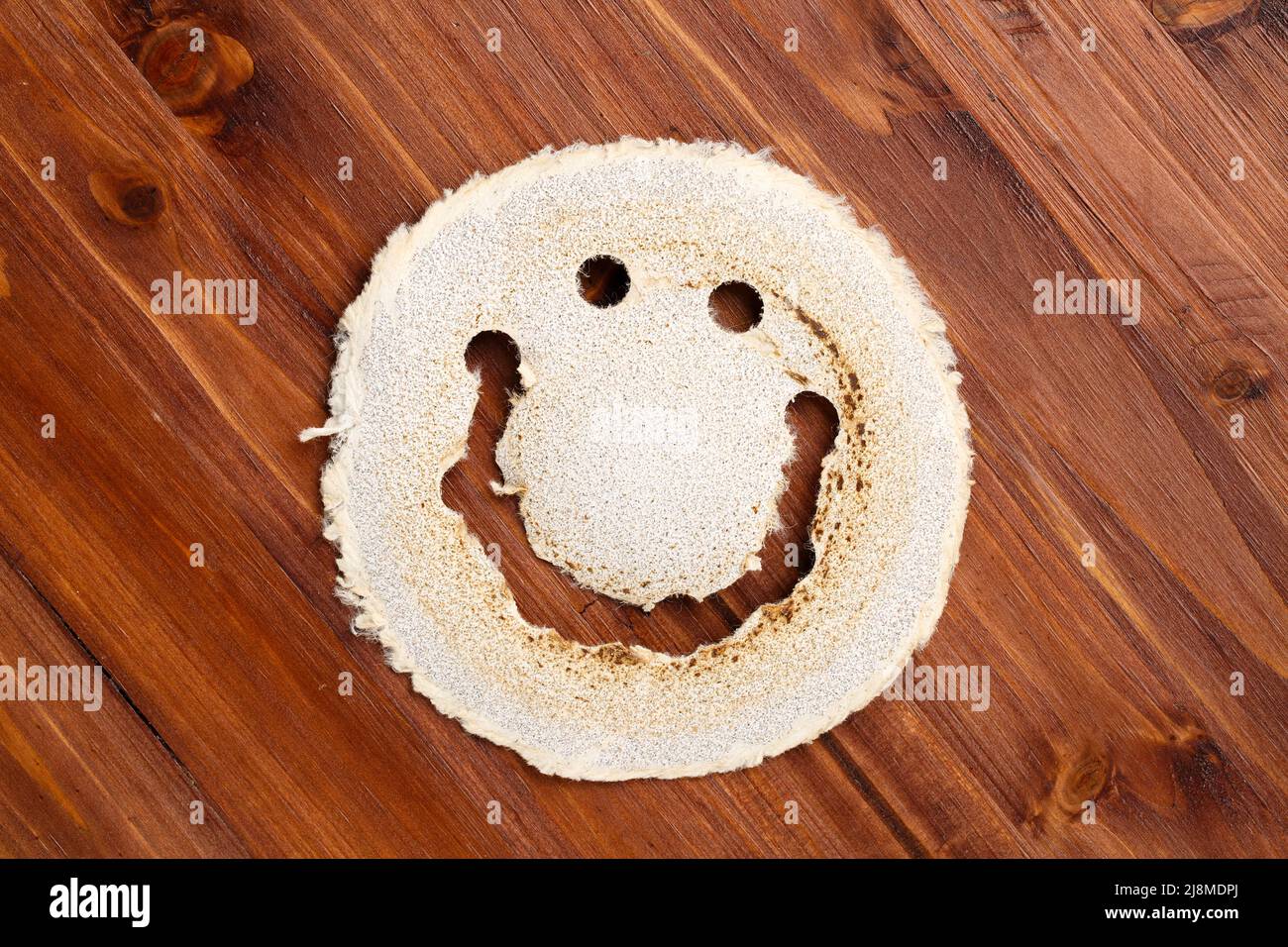 Draufsicht auf eine gebrauchte, runde Schleifpapier-Scheibe, die wie ein lächelndes Gesicht aussieht, auf einer dunklen Holzoberfläche. Umweltfreundliches Industriekonzept. Stockfoto