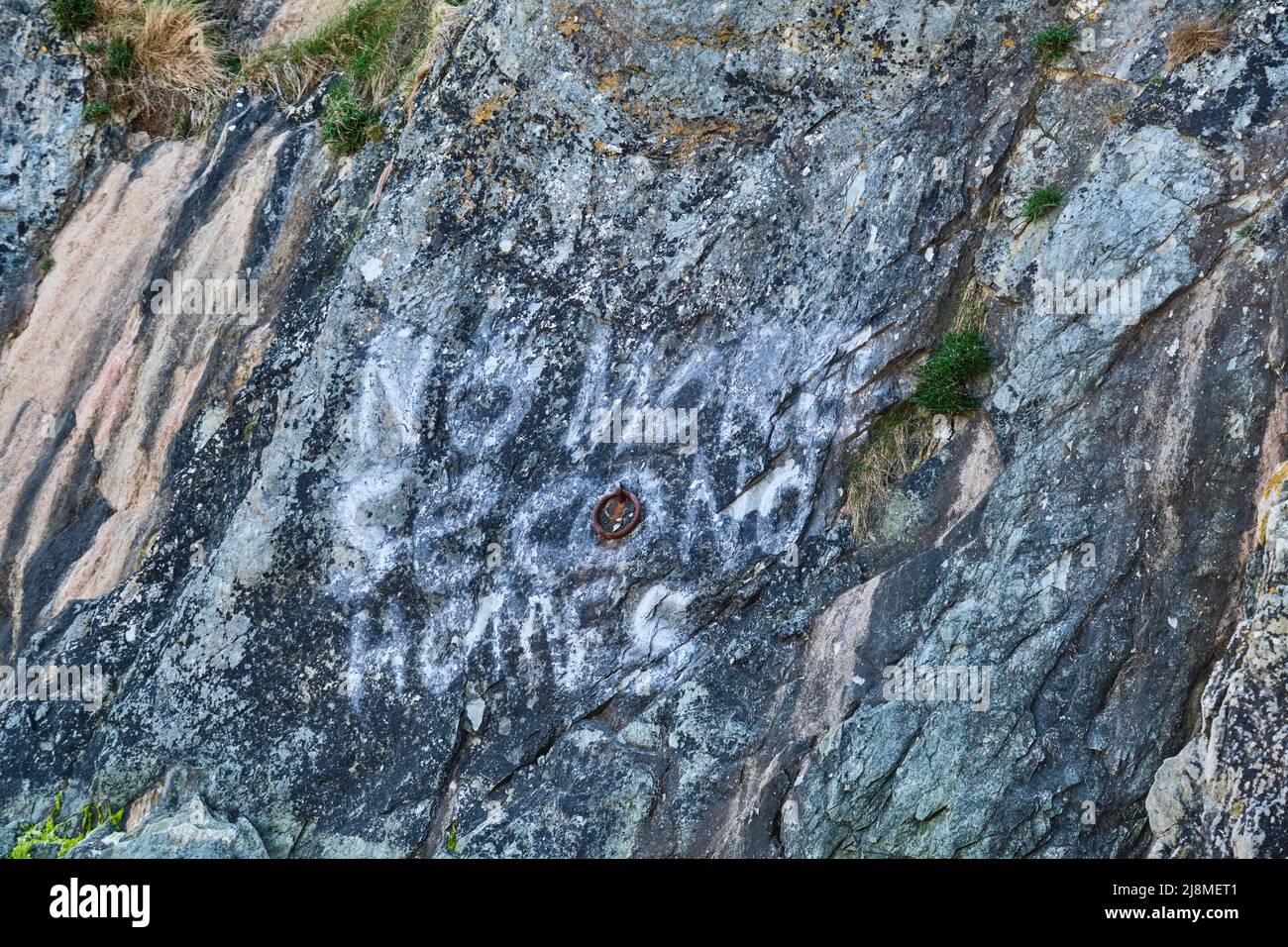 „No more second Homes“-Protest-Slogan, der in verblichener weißer Farbe auf den Küstenklippen von Port Colmon entlang des Wales Coast Path getünchten wurde Stockfoto