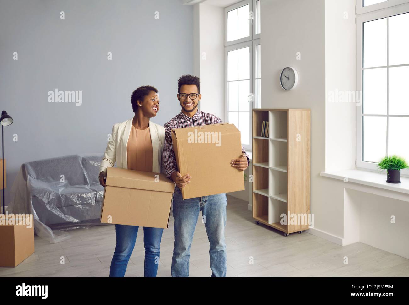 Glückliches schwarzes Paar zieht in ihr neues Haus oder ihre neue Wohnung und trägt Kisten zusammen Stockfoto