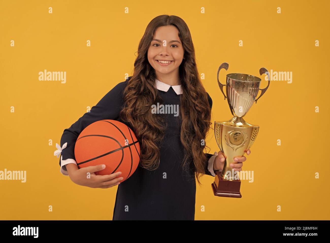 Frohes Kind halten Basketballball und Champion Cup auf gelbem Hintergrund, Sieg Stockfoto