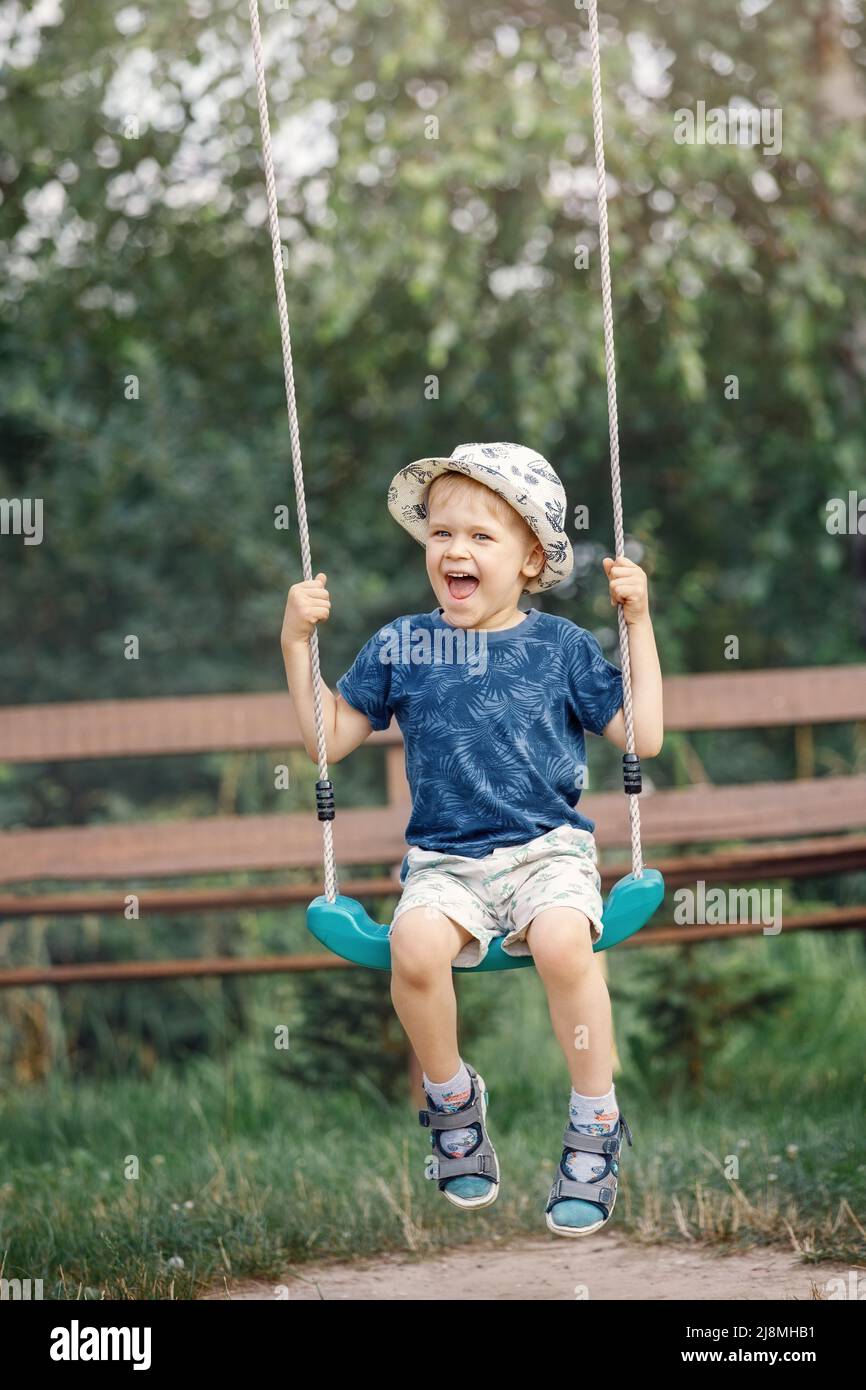 Ein süßer kleiner Junge, der sich an einem warmen und sonnigen Tag im Freien auf einer Schaukel im schönen Sommergarten amüsieren kann. Aktive Sommerferien für Kinder. Stockfoto