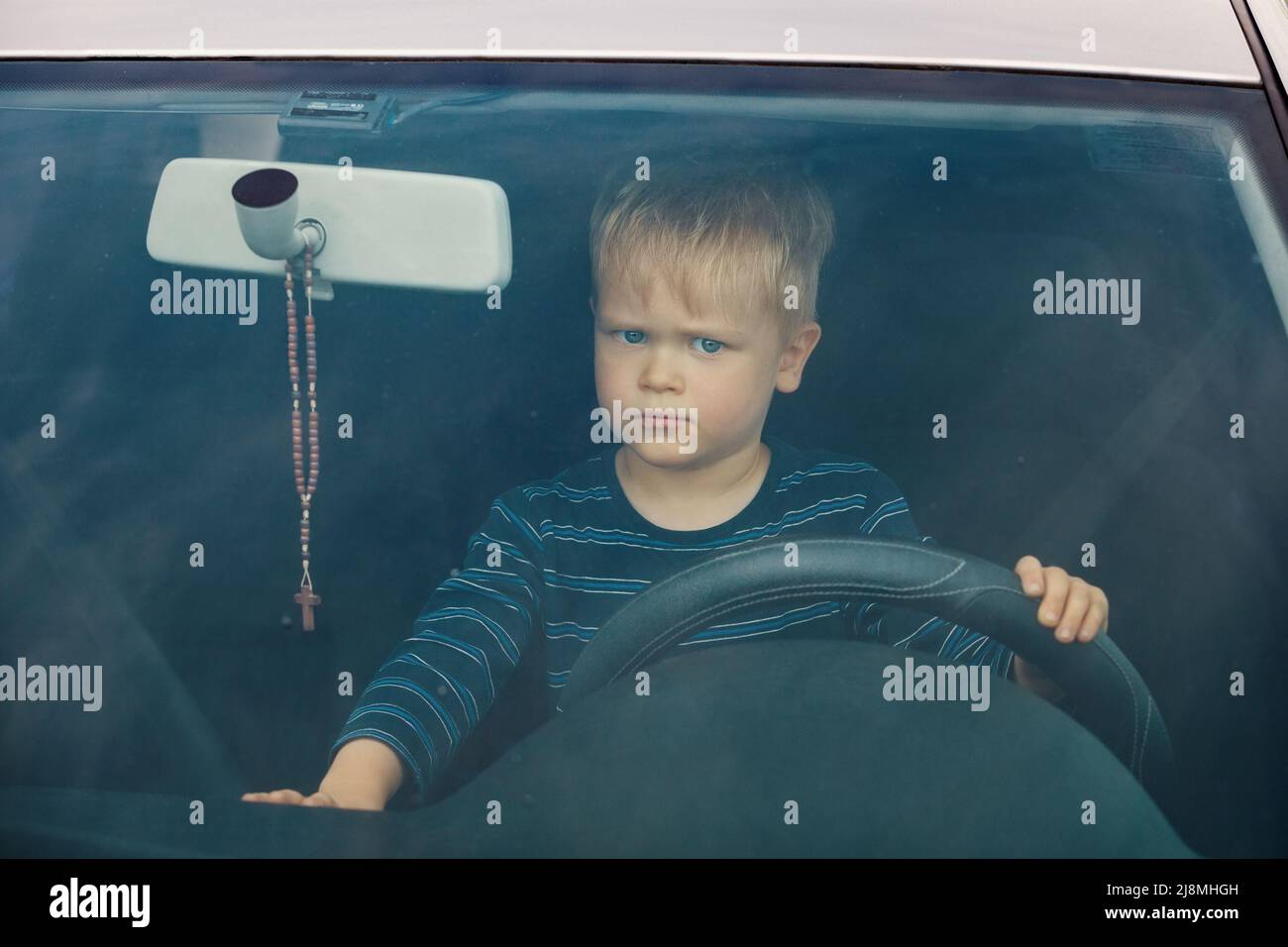 Ein ernsthafter kleiner Junge sitzt im Auto. Das Kind am Lenkrad. Stockfoto