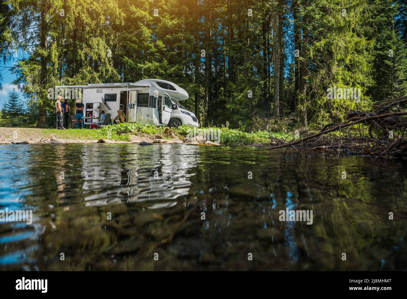 Früher Sommer Scenic Wild and Dry RV Camper Van Camping mit Freunden. Kaukasische Menschen in ihren 40s neben einem Freizeitfahrzeug und dem Fluss. Stockfoto