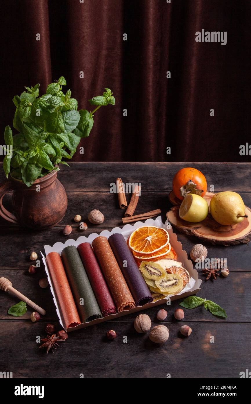 Obstpastilien verschiedener Geschmacksrichtungen und Fruchtchips oder Trockenobstscheiben in einer Geschenkbox, umgeben von frischen Früchten, Nüssen und Gewürzen und frischem Basilikum Stockfoto