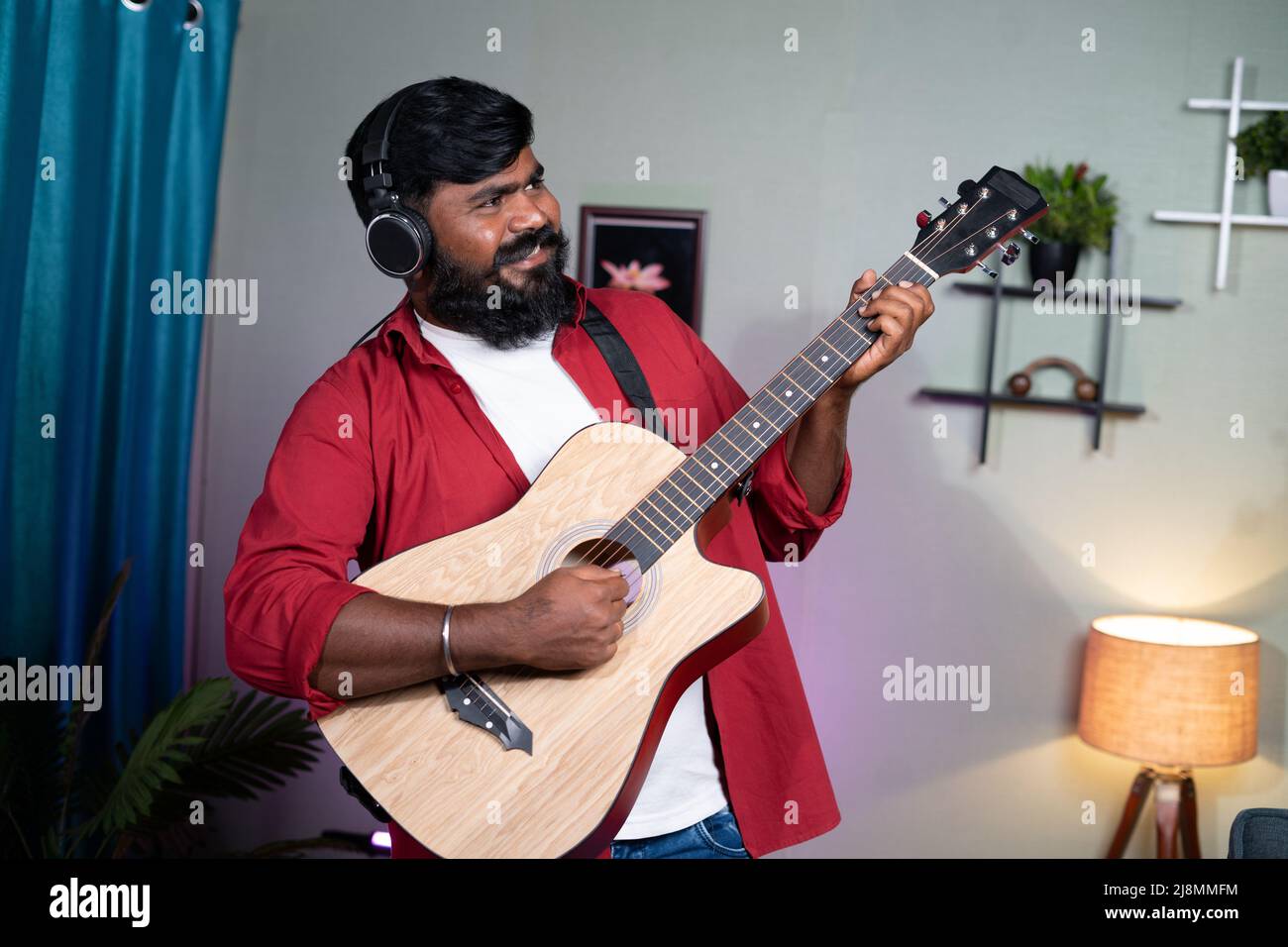 Fröhlicher junger Bartmusiker, der zu Hause Gitarre spielt - Konzept für Hobby, Entspannung am Wochenende und Freizeitaktivitäten. Stockfoto