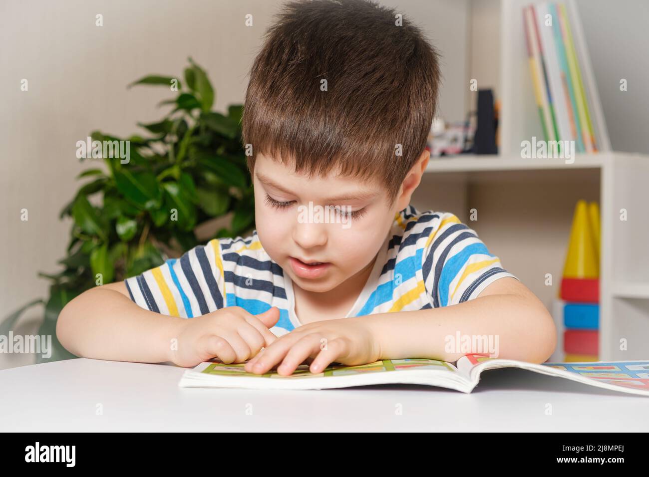 Ein 4-jähriges Kind sitzt an einem Tisch und liest ein Buch, schaut sich Bilder an, lernt lesen. Stockfoto