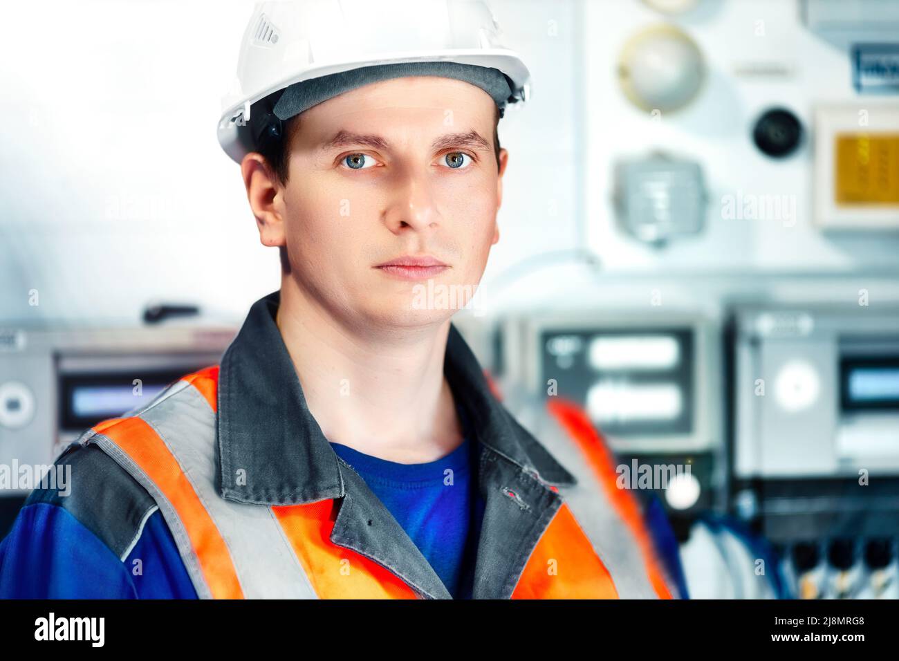 Porträt eines jungen Schwerindustrieingenieurs in Schutzweste und Arbeitskleidung und Helm. Selbstbewusster Mitarbeiter blickt direkt in die Kamera. Moderne technologische Anlage oder Produktionsanlage. Hintergrund Stockfoto