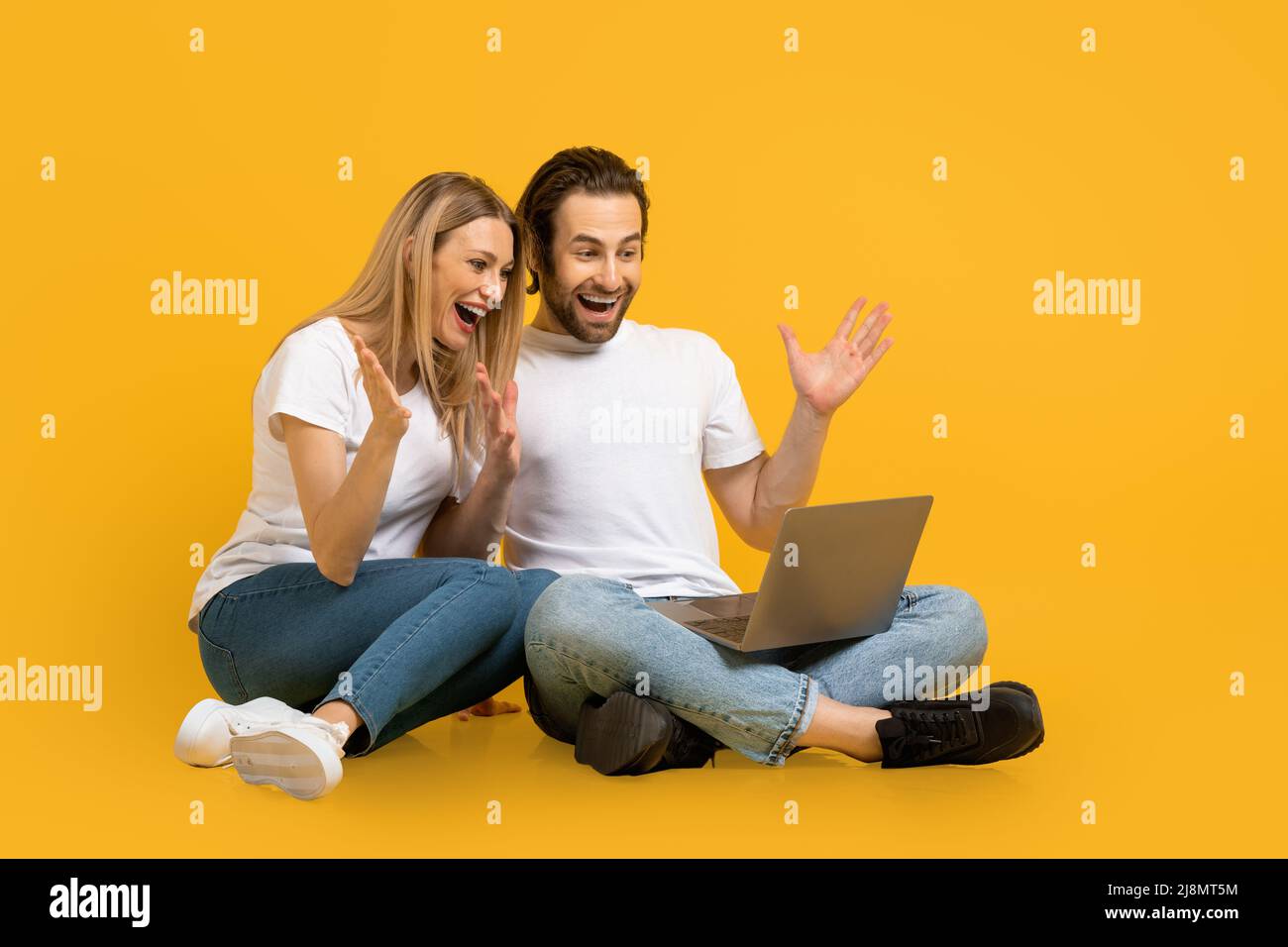 Fröhliche, überraschte junge europäische Familie sitzt auf dem Boden, schaut auf den Laptop, gestikuliert Stockfoto
