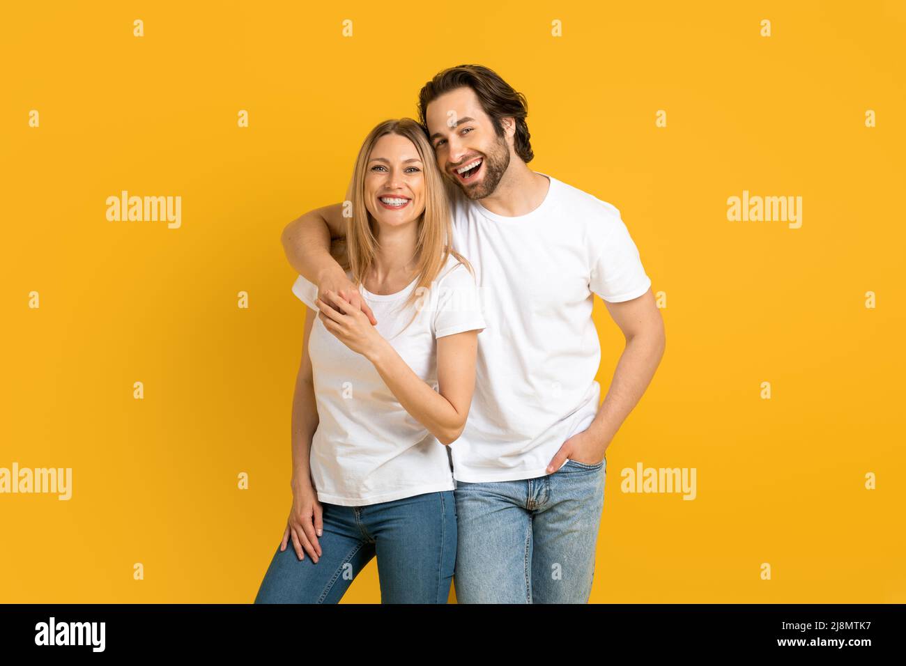 Fröhlicher junger europäer in weißen T-Shirts umarmt, viel Spaß, isoliert auf gelbem Hintergrund Stockfoto