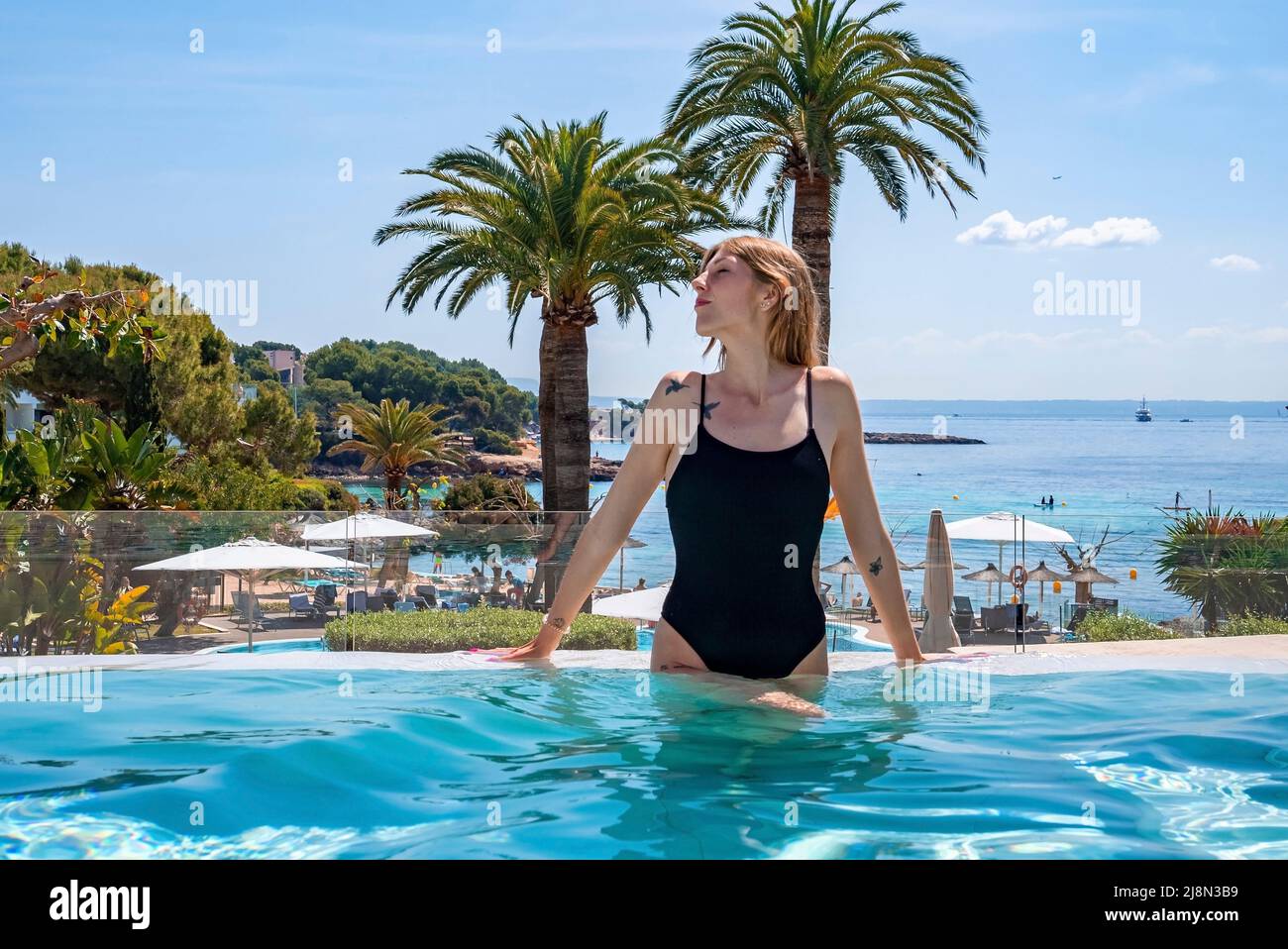 Junge Frau, die sich an sonnigen Tagen im Pool des Hotel-Spa gegen das Meer entspannt Stockfoto