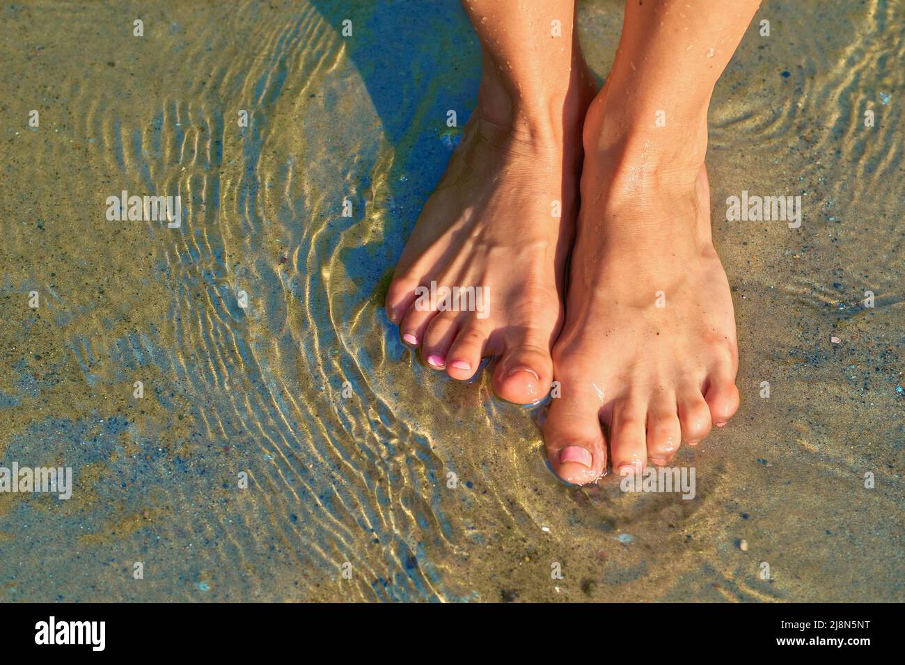 Die Beine des niedlichen Mädchens stehen in klarem, transparentem Wasser Stockfoto