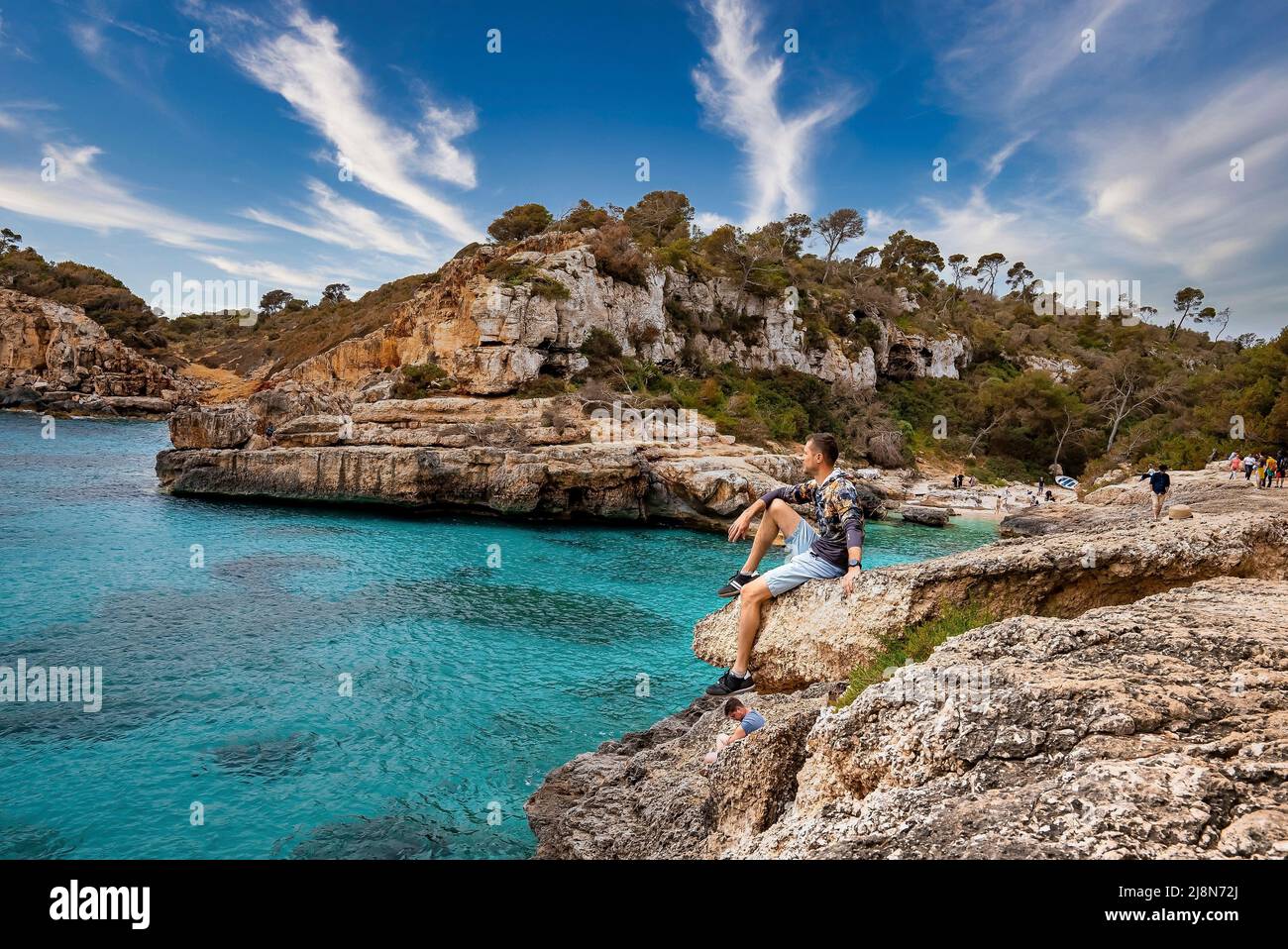 Männlicher Tourist, der sich auf felsigen Klippen entspannt, während er die Küste gegen den Himmel betrachtet Stockfoto