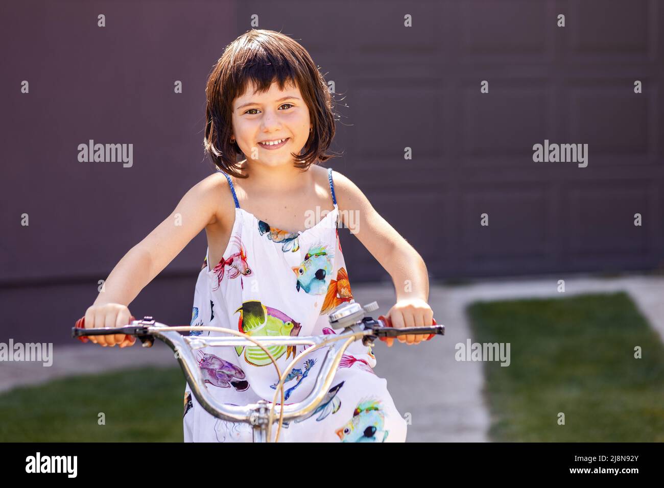 Glückliches kleines Mädchen, das Fahrrad auf einer Gasse reitet, während es die Kamera anschaut und lächelt Stockfoto