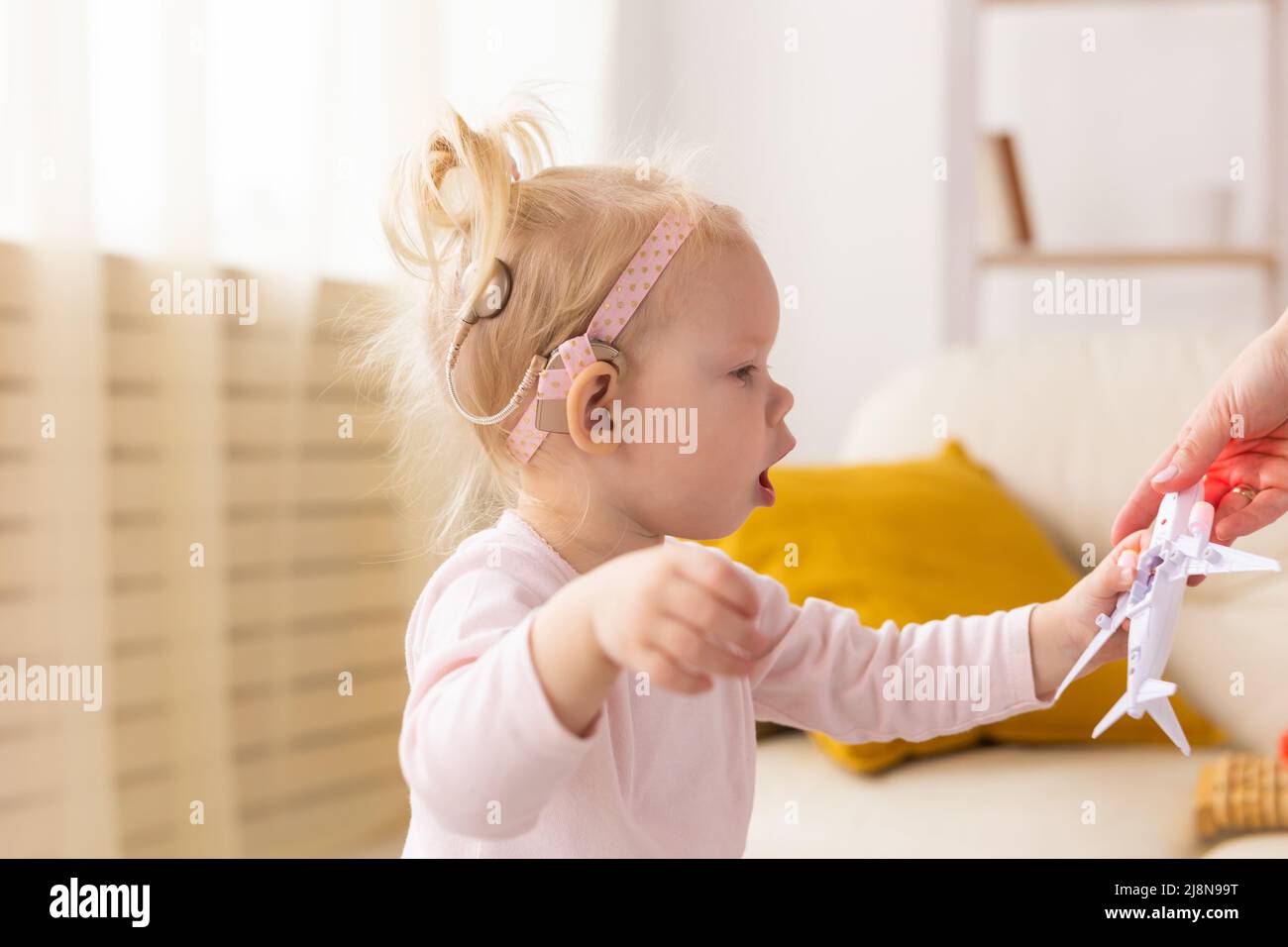 Cochlea-Implantat für Babys. Taubes Kind mit Hörgerät spielt im Wohnzimmer Stockfoto