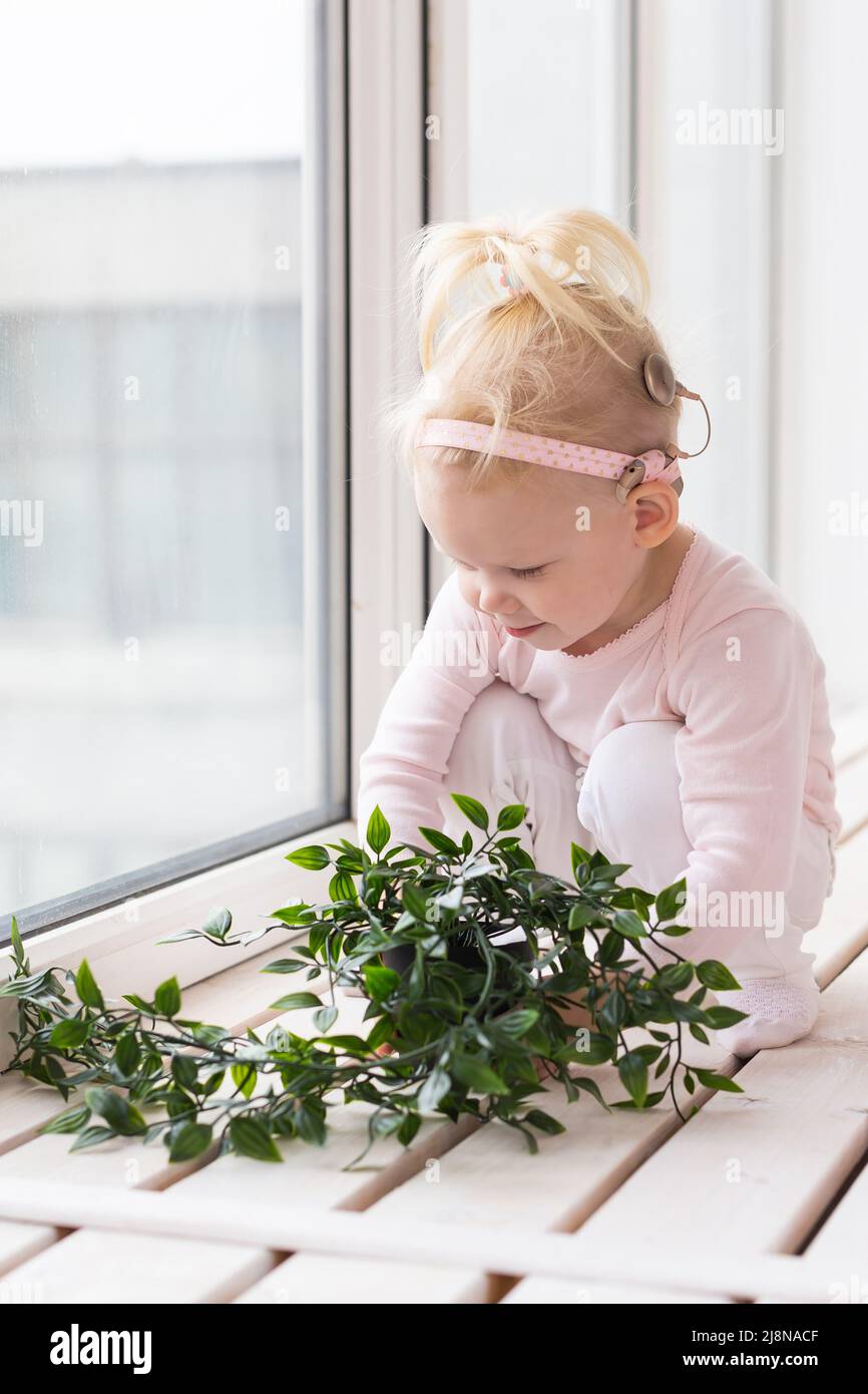 Baby mit Cochlea-Implantat sitzt zu Hause und isst. Hören Sie, wie die Hilfe und die Medizin innovative Technologien entwickeln Stockfoto