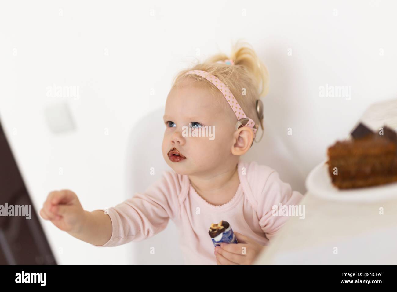Cochlea-Implantat für Babys. Taubes Kind mit Hörgerät spielt im Wohnzimmer Stockfoto