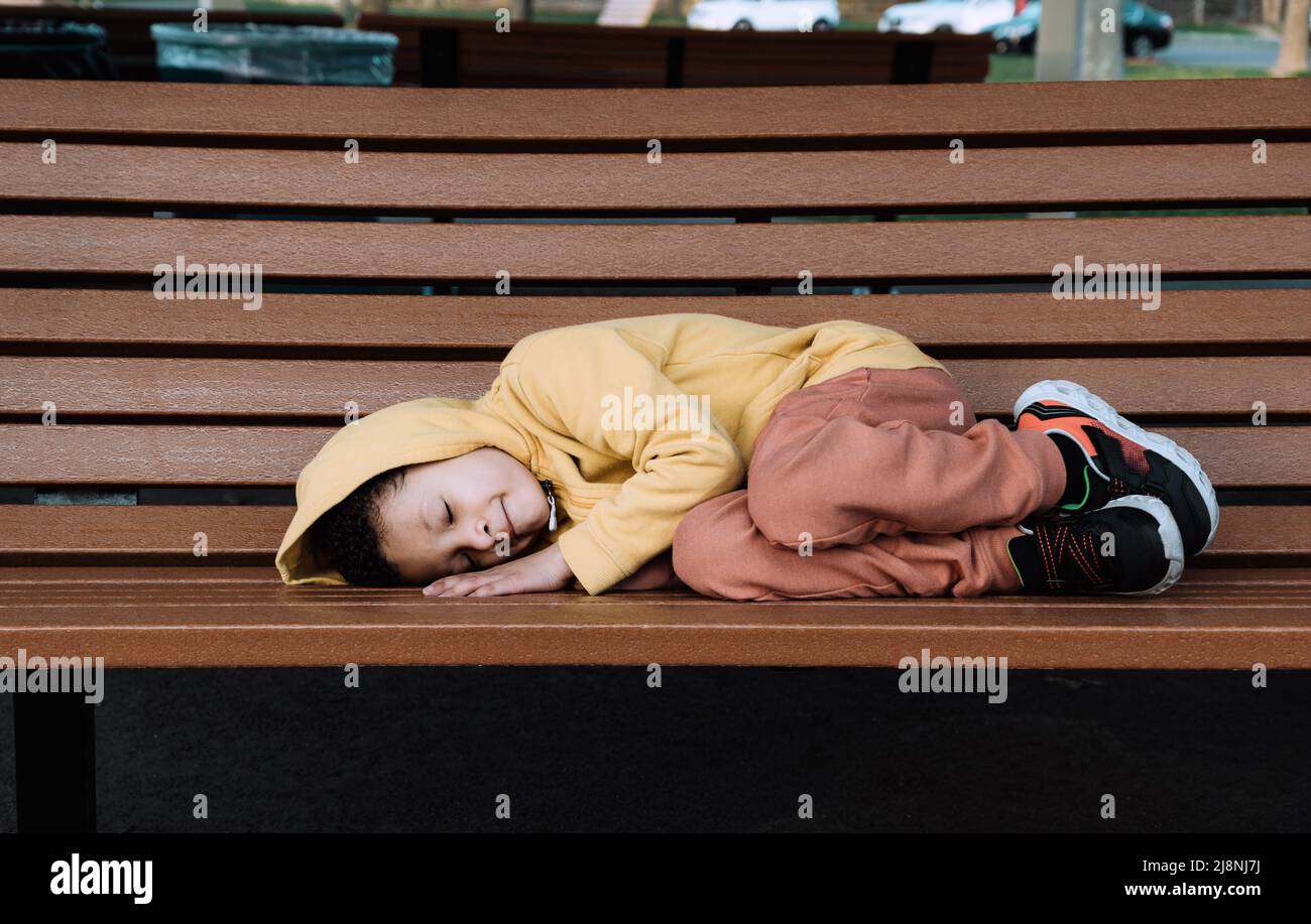 Traurig allein liegt der kleine Junge auf einer Bank in einem öffentlichen Park. Kopierbereich Stockfoto