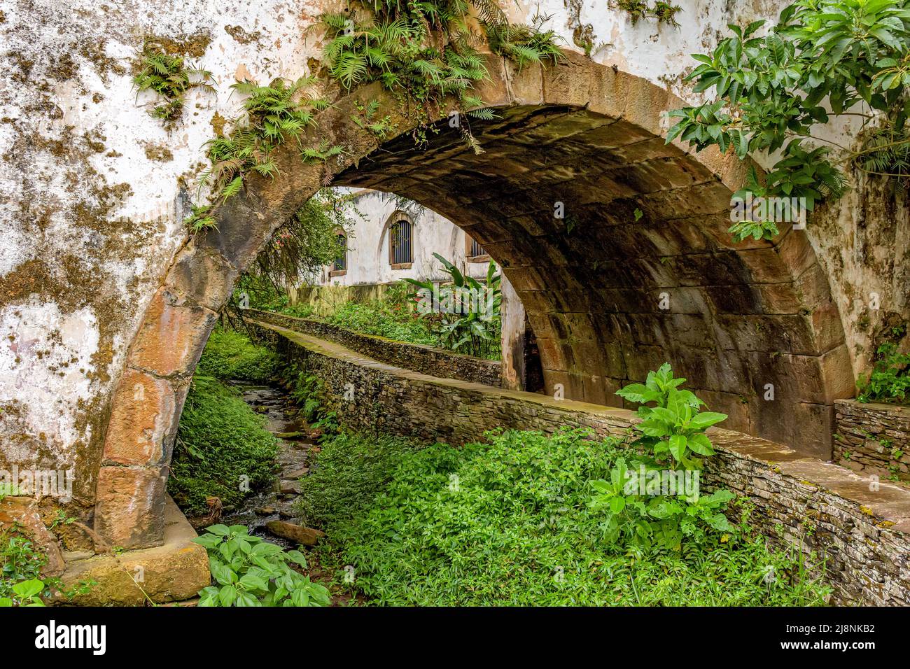 Alter historischer Steintunnel, der durch Vegetation und alte Häuser im Kolonialstil in der historischen Stadt Ouro Preto im Bundesstaat Minas Gerais führt. Stockfoto