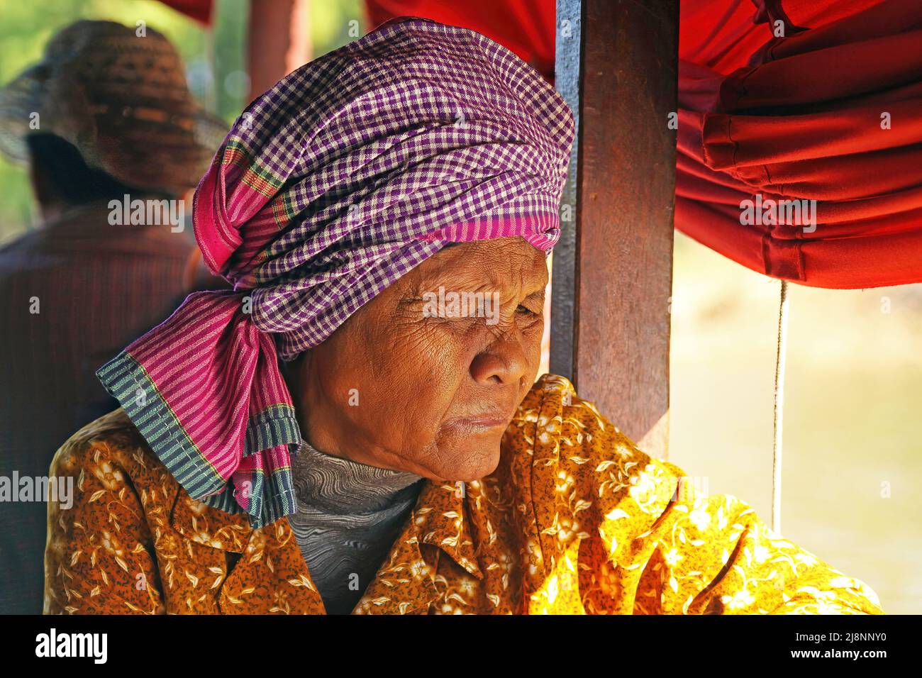 Siem Reap, Kambodscha - Dezember 9. 2019: Porträt einer alten, wanderenden, zerknitterten khmer-Frau mit traditioneller Krama-Kopfbandanna, die in der Sonne nachdenklich aussieht Stockfoto