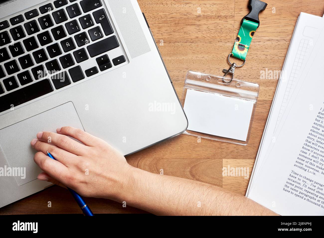 Ansicht von oben auf einen Schreibtisch, eine unbekannte Person, die studiert oder arbeitet, einen Laptop, bedruckte Blätter und einen leeren Personalausweis mit einem Trageband aus Sonnenblumen, Symbol für p Stockfoto