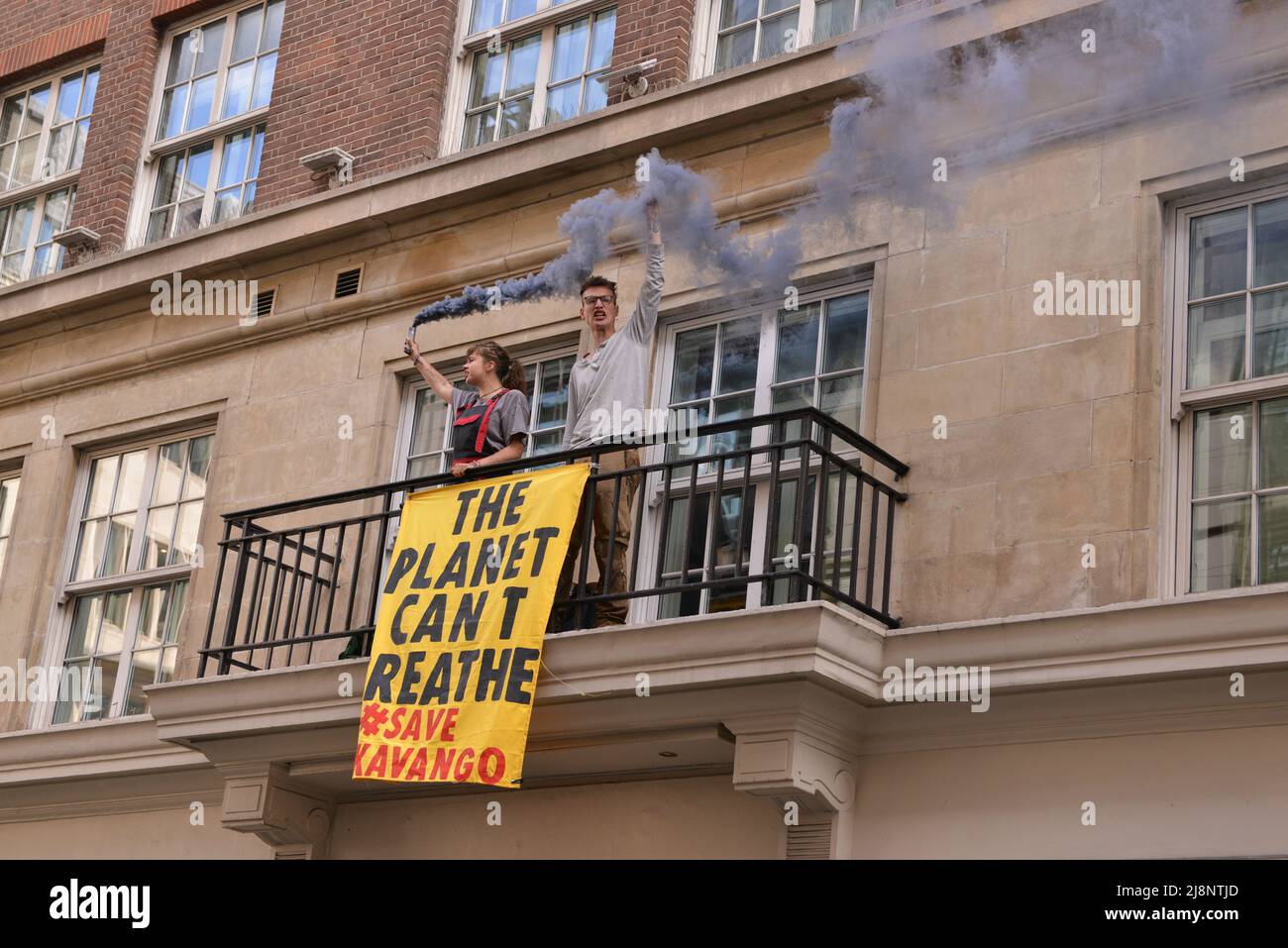 Aktivisten halten eine Rauchfackel und ein Banner auf dem Balkon des May Fair Hotels. Aktivisten des Extinction Rebellion stürmen das May Fair Hotel im Zentrum von London aus Protest gegen einen Ölgipfel (Africa Energies Summit), der im fünf-Sterne-Hotel stattfindet. Stockfoto