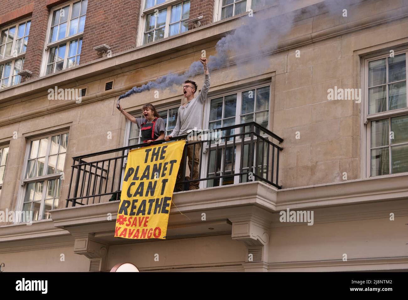 Aktivisten halten eine Rauchfackel und ein Banner auf dem Balkon des May Fair Hotels. Aktivisten des Extinction Rebellion stürmen das May Fair Hotel im Zentrum von London aus Protest gegen einen Ölgipfel (Africa Energies Summit), der im fünf-Sterne-Hotel stattfindet. Stockfoto