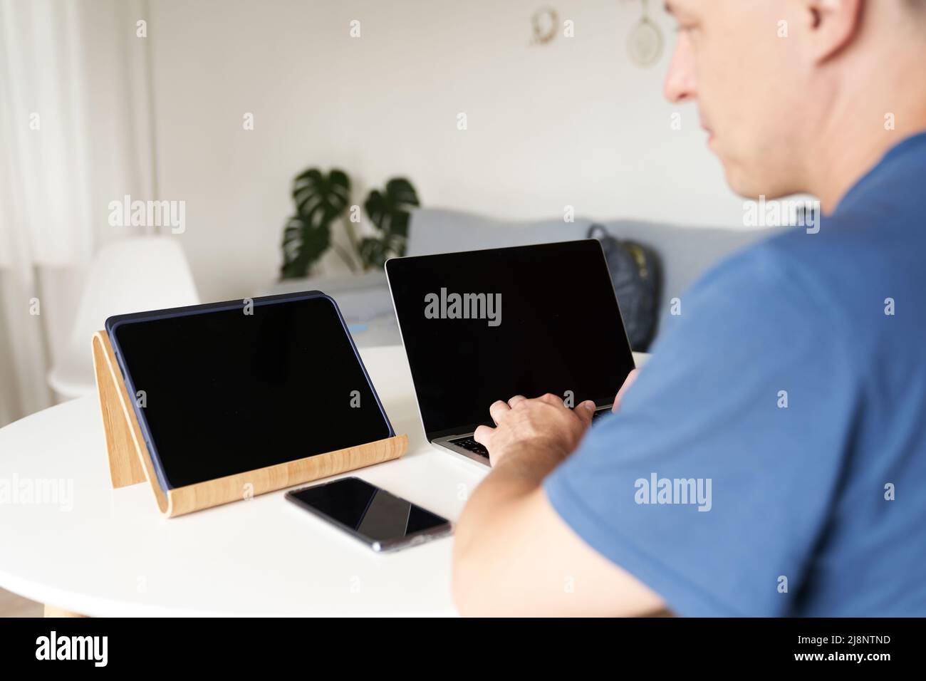 Eine seriöse Person, die zu Hause aus der Ferne arbeitet. Ein Mann gibt Informationen in einen Laptop ein. Layout-Konzept, Design. Schwarze Bildschirme auf Laptops und Tablets. Layout für Ihr Design. Hochwertige Fotos Stockfoto
