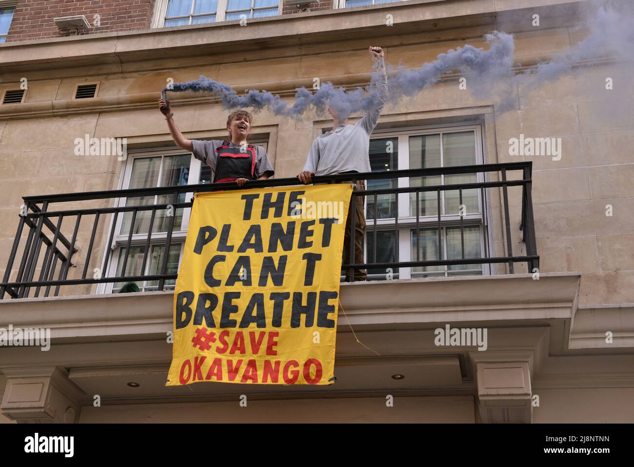 Aktivisten halten eine Rauchfackel und ein Banner auf dem Balkon des May Fair Hotels. Aktivisten des Extinction Rebellion stürmen das May Fair Hotel im Zentrum von London aus Protest gegen einen Ölgipfel (Africa Energies Summit), der im fünf-Sterne-Hotel stattfindet. Stockfoto