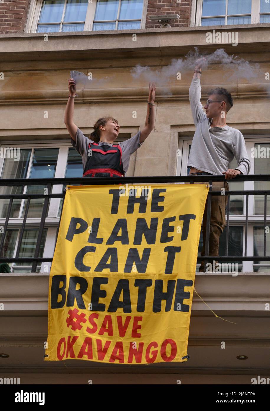 Aktivisten halten eine Rauchfackel und ein Banner auf dem Balkon des May Fair Hotels. Aktivisten des Extinction Rebellion stürmen das May Fair Hotel im Zentrum von London aus Protest gegen einen Ölgipfel (Africa Energies Summit), der im fünf-Sterne-Hotel stattfindet. Stockfoto