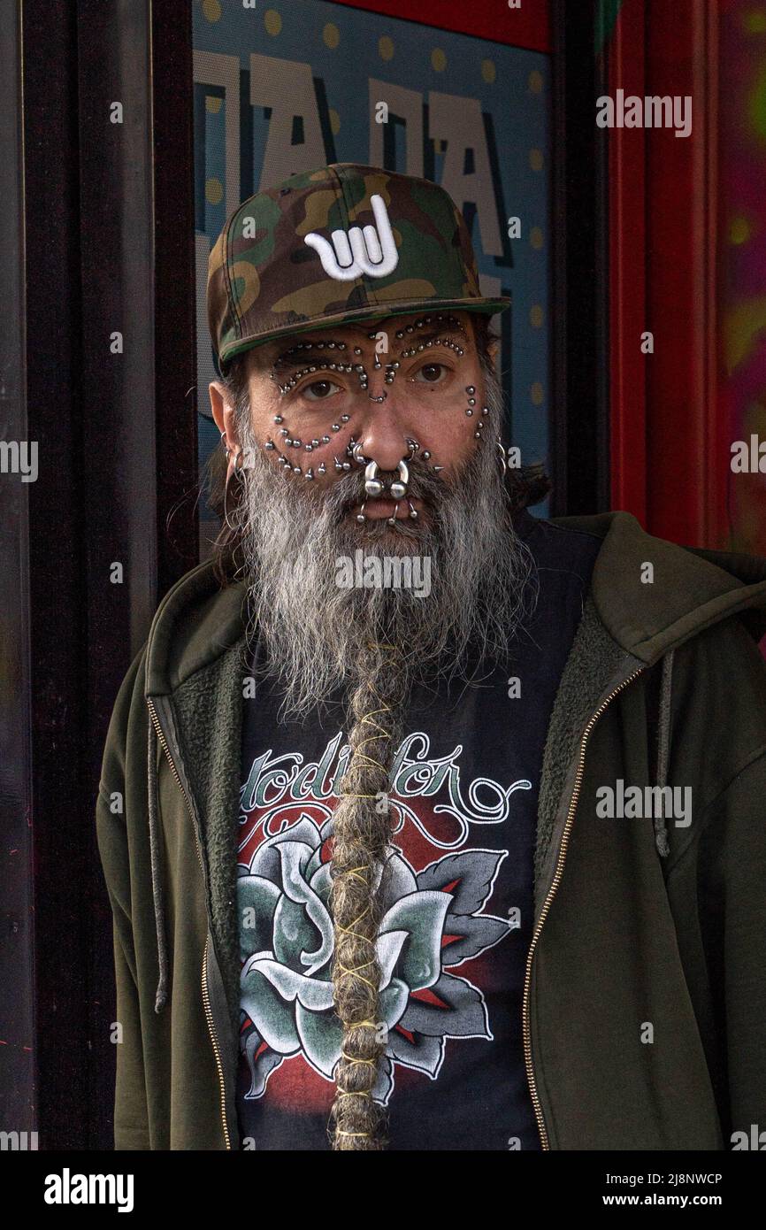Schwer durchbohrter Mann mit einem langen grauen geflochtenen Bart, lässig gekleidet, steht in einer Tür Stockfoto