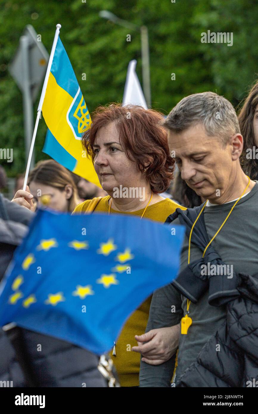 Eine Frau mittleren Alters geht in einer Menschenmenge mit einer mittelgroßen ukrainischen Flagge, die in ihrer Hand angehoben ist, und der Flagge der Europäischen Union vor ihr Stockfoto