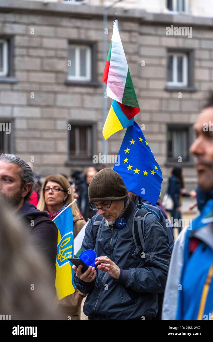 Ein Mann auf der Straße hält Flaggen der Ukraine, Bulgariens und der EU und schaut in seinem Smartphone auf den Support Ukraine march Stockfoto