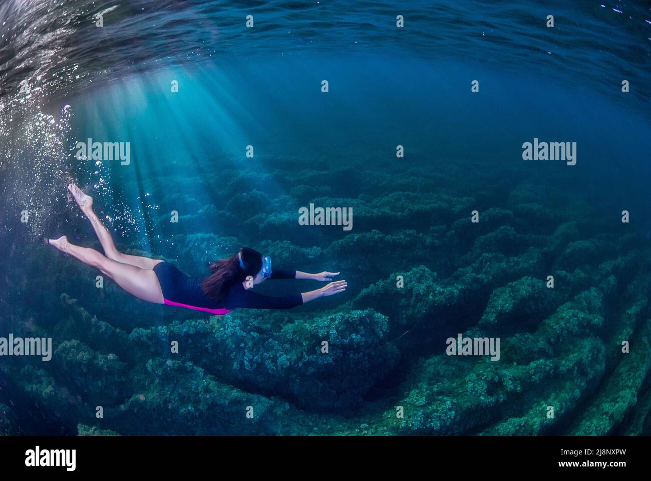 Frau, die im Mittelmeer unter Wasser schwimmend ist. Lichtstrahlen, die von links in das Wasser eindringen. Stockfoto